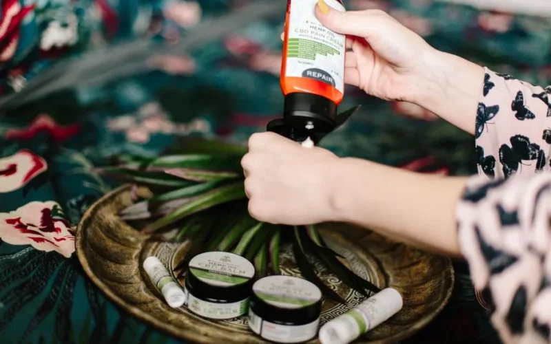 Close-up shot of a woman applying CBD lotion, surrounded by wellness products on a decorative plate.