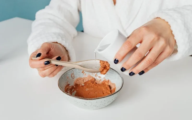 Close-up of a person mixing a natural clay mask with water for skincare.