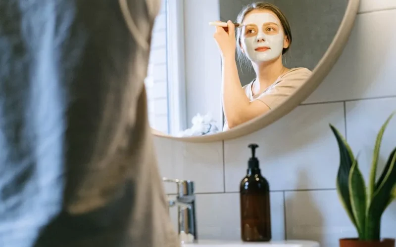 A woman applies a clay mask using a brush, promoting skincare and self-care routines.