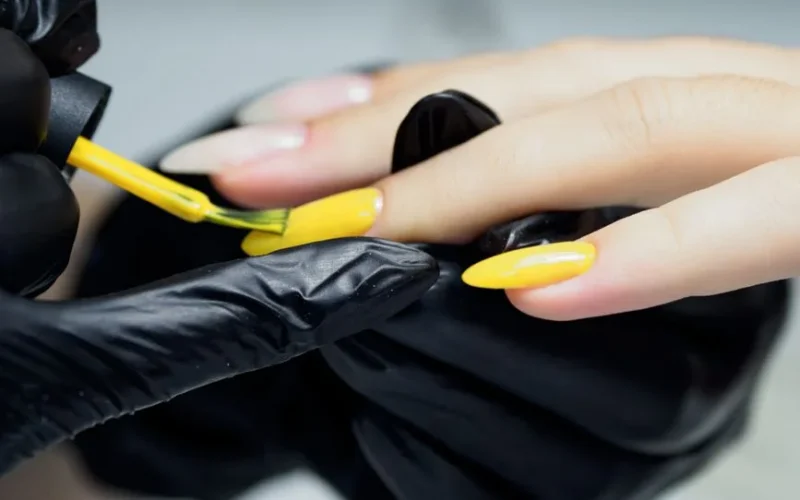 Closeup of a beautician applying yellow nail polish, showcasing precision and care.