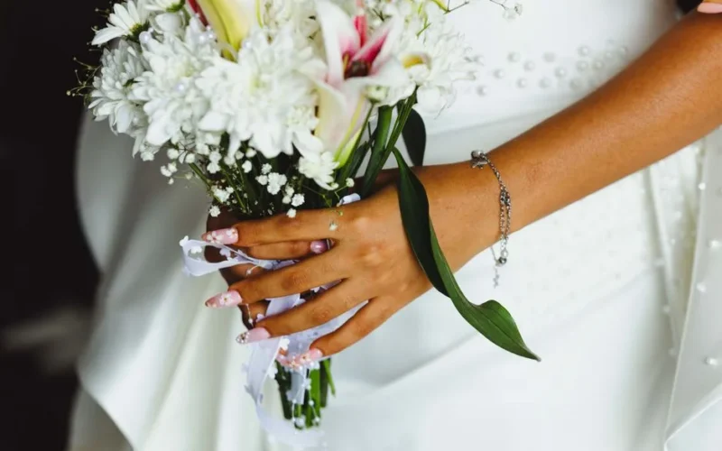 Close-up of a bridal bouquet with woman's hand showing manicured nails and bracelet.