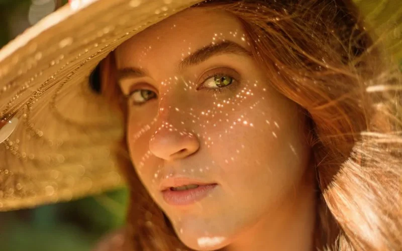 Close-up of a young woman with a straw hat creating a warm shadow effect.