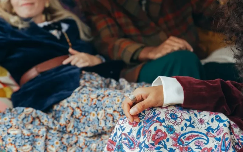 Close-up of a group wearing retro floral and plaid clothing, seated in a relaxed indoor setting.