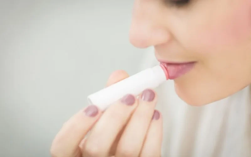 A woman applies lip balm for moisturizing her lips, focusing on health and beauty.