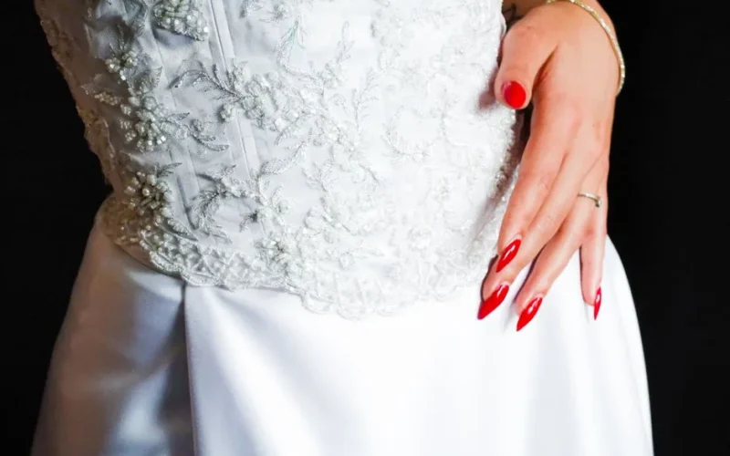 Close-up of elegant white lace wedding dress with intricate patterns and red nails.