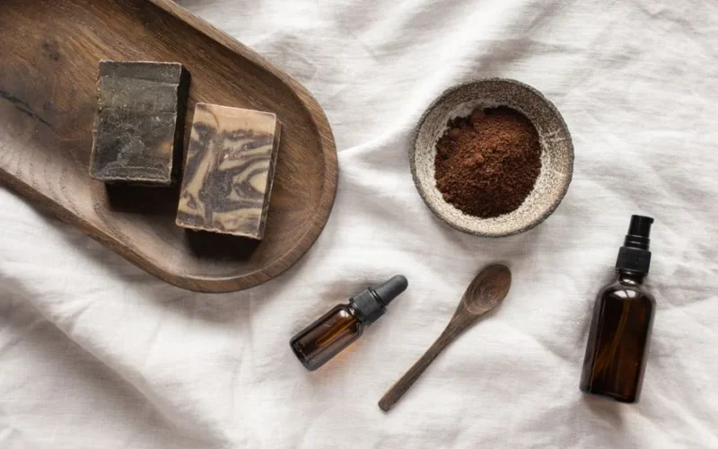 Top view of coffee scrub in bowl composed with bottles of aromatic oil on white sheet
