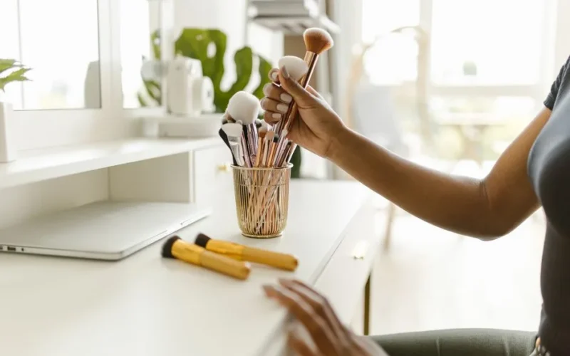 A woman organizing makeup brushes on a white dresser in a bright and modern room.