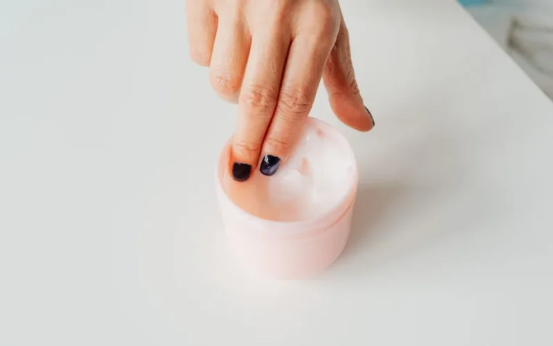Close-up of a hand with painted nails dipping into a jar of face cream, representing self-care.