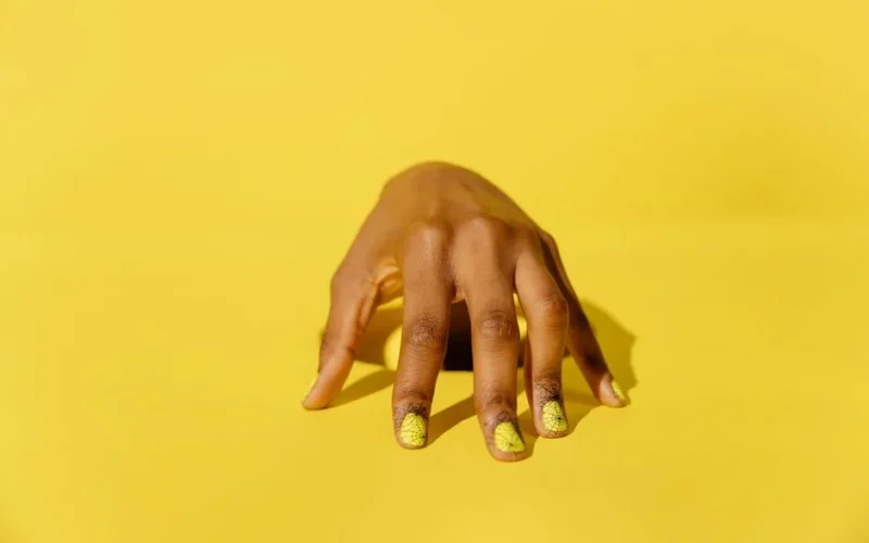 Stylish yellow nail art on a hand against a vibrant yellow background, perfect for beauty and fashion themes.