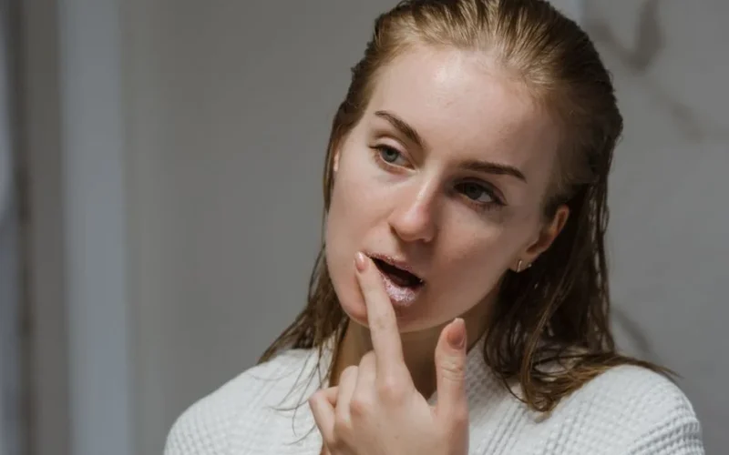 Adult woman applying a lip scrub as part of her beauty routine indoors.