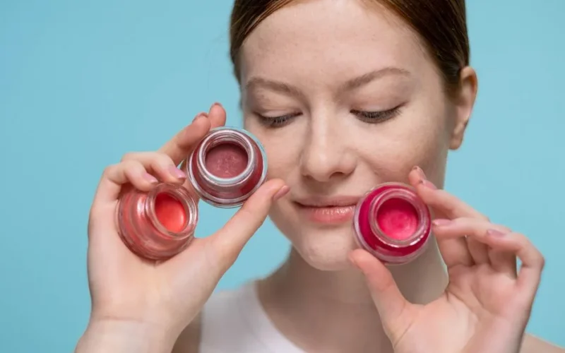 Close-up portrait of a woman holding colorful lip balm jars showcasing skincare and beauty products.