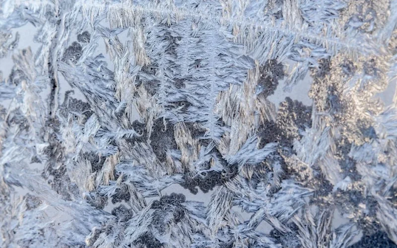 Close-up of frosty ice crystals forming intricate patterns on a window during winter.