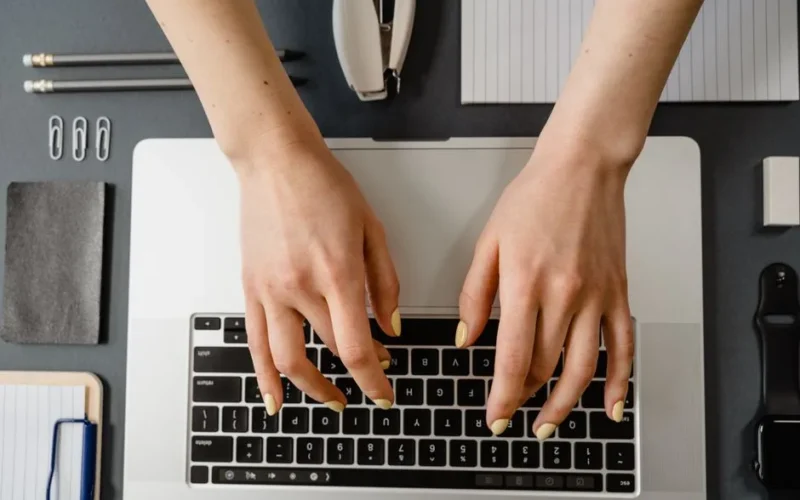 Close-up of woman's hands with manicured nails typing on a laptop.