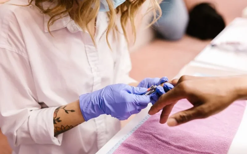 Cosmetologist performing a manicure in a spa using precision tools and gloves.