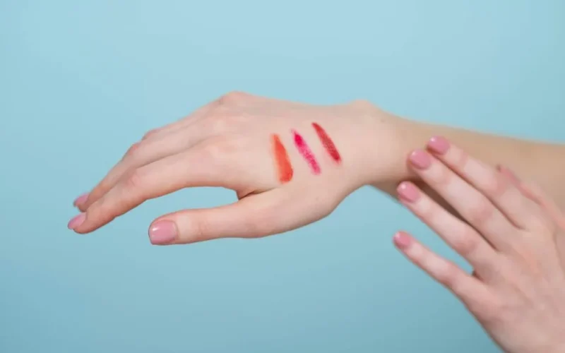Close-up of lipstick swatches on a woman's hand against a blue background.
