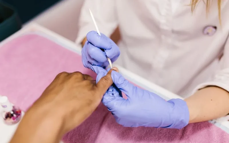 Manicurist performs cuticle care during a manicure session in a salon setting.
