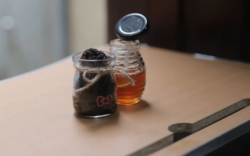 Close-up of glass jars with honey and body scrub, set on a wooden table, showcasing natural skincare ingredients.