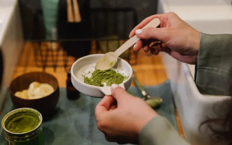 Close-up of hands blending green powder for beauty treatment in a home setting.
