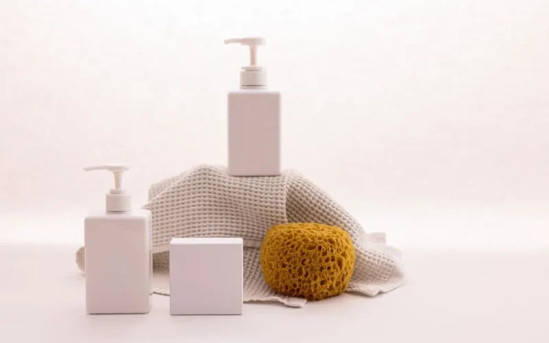 White pump bottles with a natural sponge on a textured cloth, ideal for beauty product mockups.
