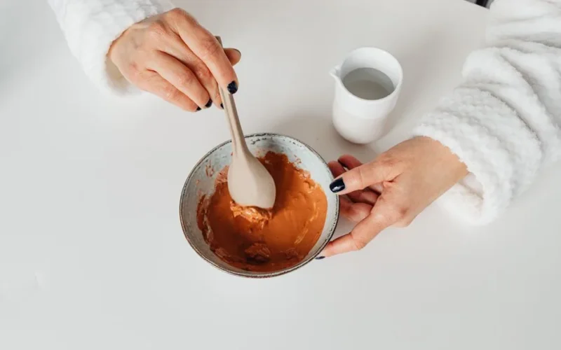 Top view of a woman mixing a skincare mask with a spoon in a bowl, highlighting a beauty routine.