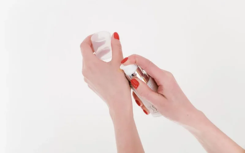 Close-up of woman's hands with red manicure applying moisturizer on white background.