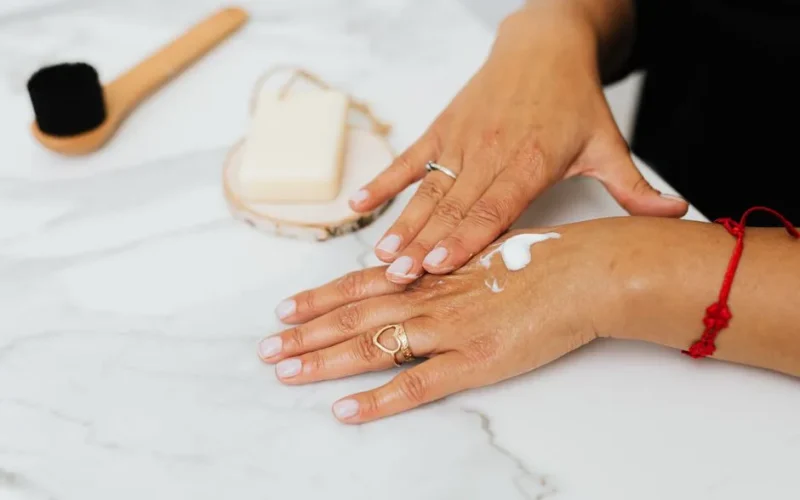 Close-up of a woman applying moisturizer to her hands with care products nearby.
