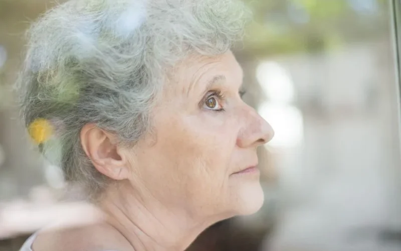 Close-up of an elderly woman with gray hair looking thoughtfully through a window.