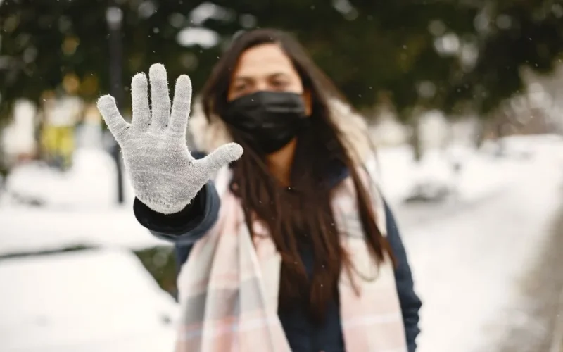 A woman in winter attire wearing a mask and glove outside in the snow.