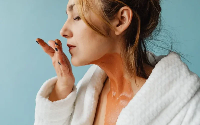 Woman in bathrobe applying face mask. Close-up wellness skincare routine.