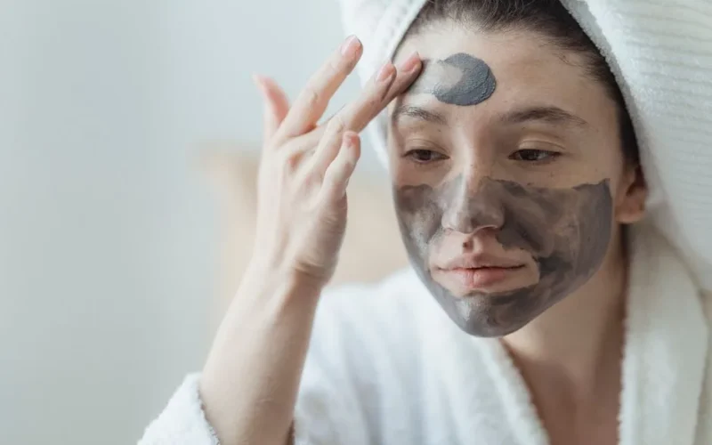 Adult woman relaxing with a clay face mask, enhancing skin health and wellness indoors.