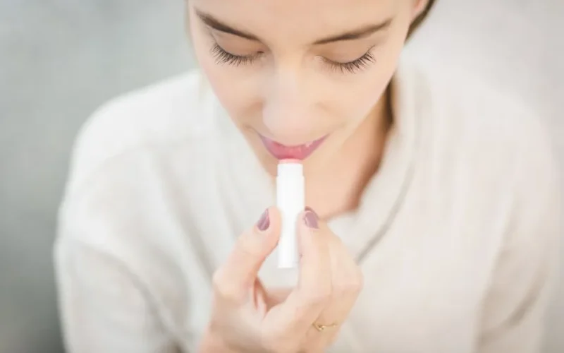 A close-up of a woman applying light-colored lip balm for moisturizing.