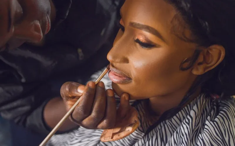 Detailed close-up of a makeup artist applying lipstick to a bride's lips, showcasing precision and artistry.