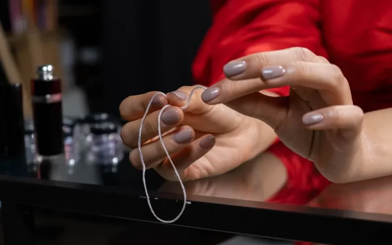 Close-up of manicured hands entwining thread, showcasing nail art and fashion.