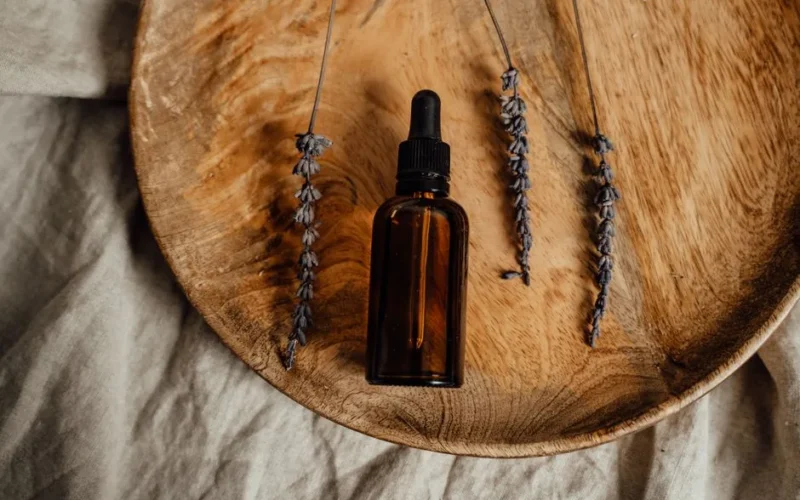 Brown glass dropper bottle with dried lavender on wooden platter, ideal for skincare promotions.