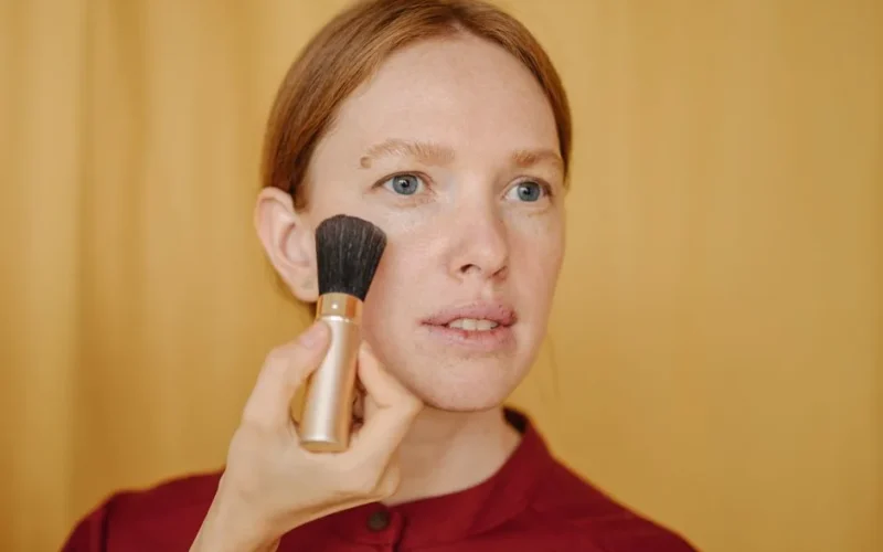 Close-up of a woman applying makeup with a brush in a studio setting.