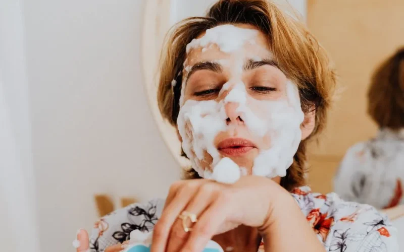 Close-up of a woman applying foamy facial wash, embracing self-care indoors.