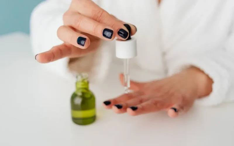 Close-up of a woman applying skincare serum with a dropper to her hand.
