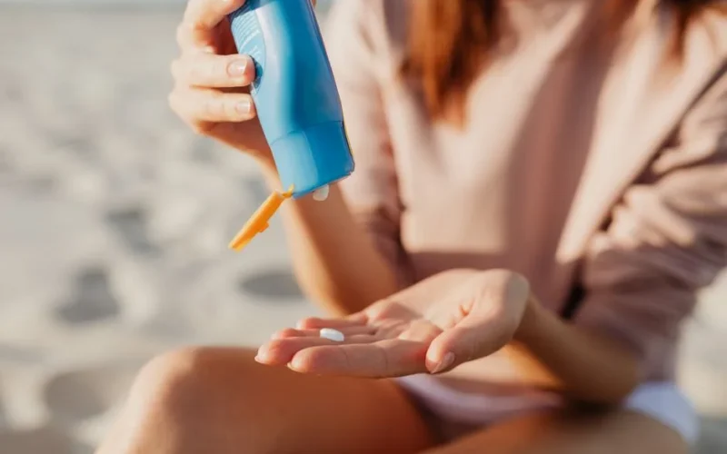 A person applies sunscreen at the beach on a sunny day.