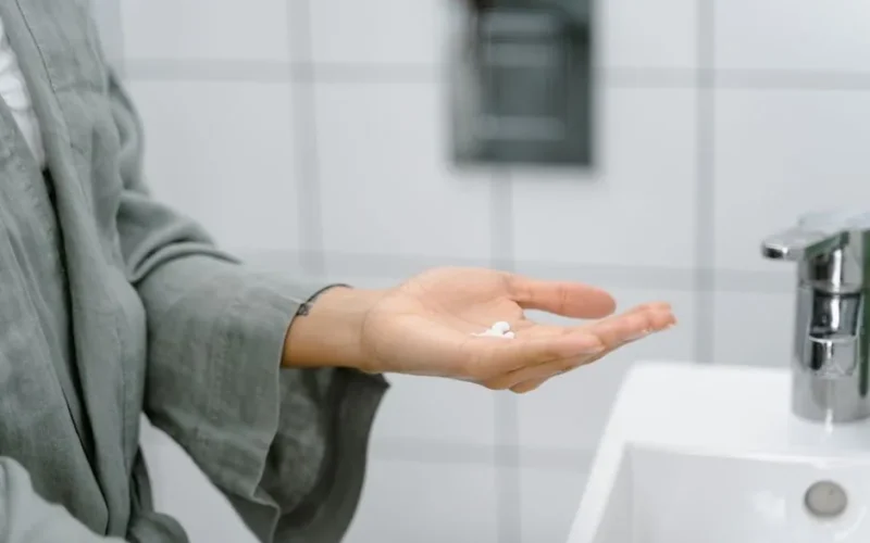 A close-up of a hand holding cream near a modern bathroom sink.