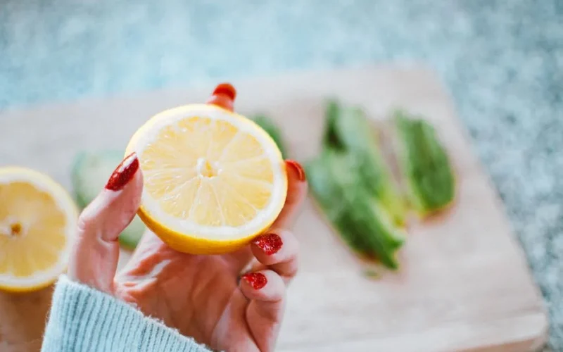 Close-up of a hand with red nails holding a fresh sliced lemon, perfect for culinary or health-themed projects.