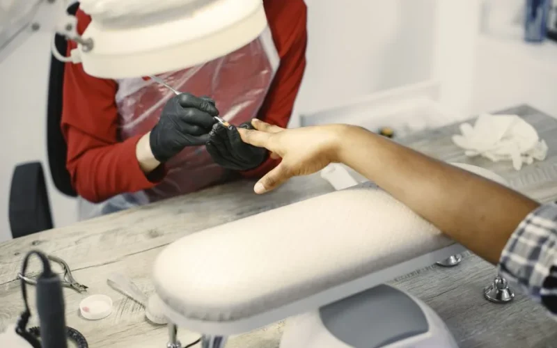 Close-up of a manicurist painting nails in a modern beauty salon with gloves on.