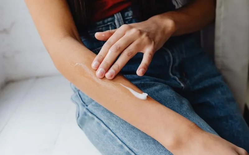 Detailed close-up of a person applying cream to their arm for skincare routine.