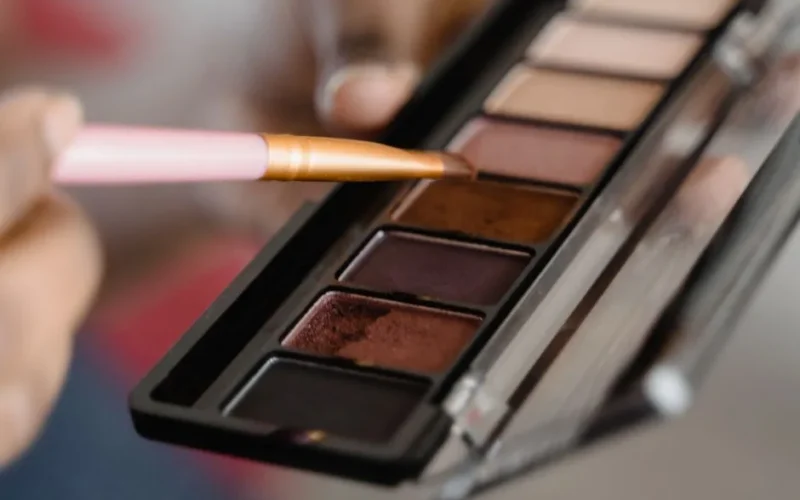 A detailed close-up of an eyeshadow palette with a makeup brush in use.