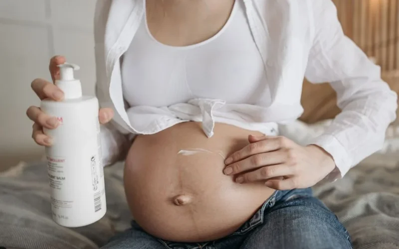 Close-up of a pregnant woman applying moisturizing lotion to her belly for skincare and maternity care.