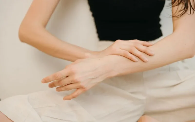 Close-up of a woman applying cosmetic cream on her arm for skincare.