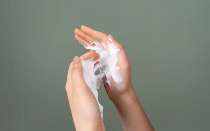 Close-up of hands applying rich moisturizing cream on a green background.