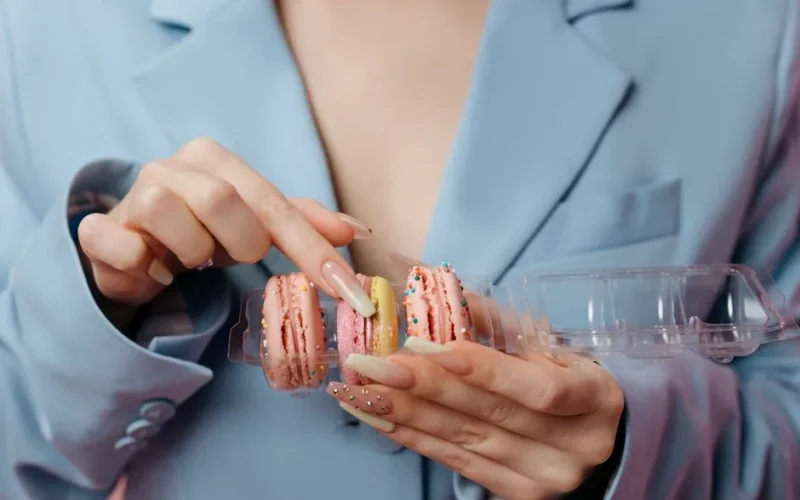 Close-up of hands holding colorful French macarons, highlighting manicured nails.