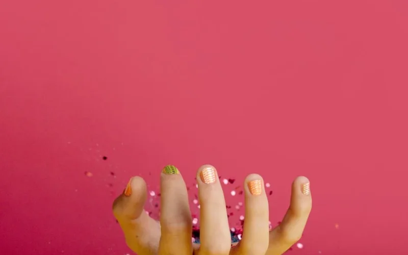 Detailed view of a hand showcasing colorful manicure against a vibrant pink backdrop, offering ample copy space.