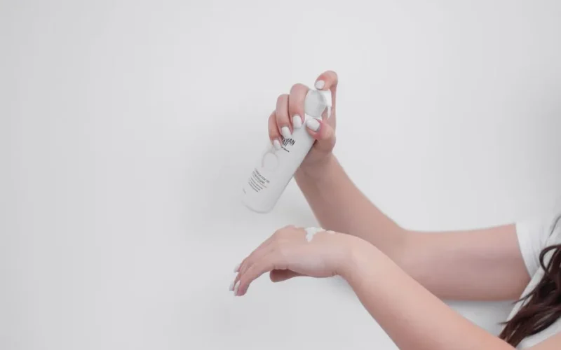 Close-up of woman's hands applying white hand cream against a white backdrop.