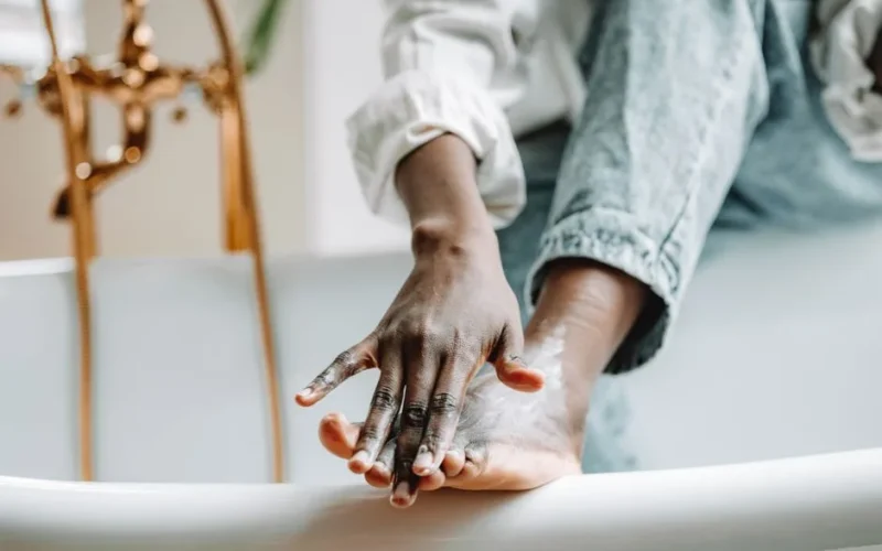 Focused view of a person applying foot cream while sitting on a bathtub edge.